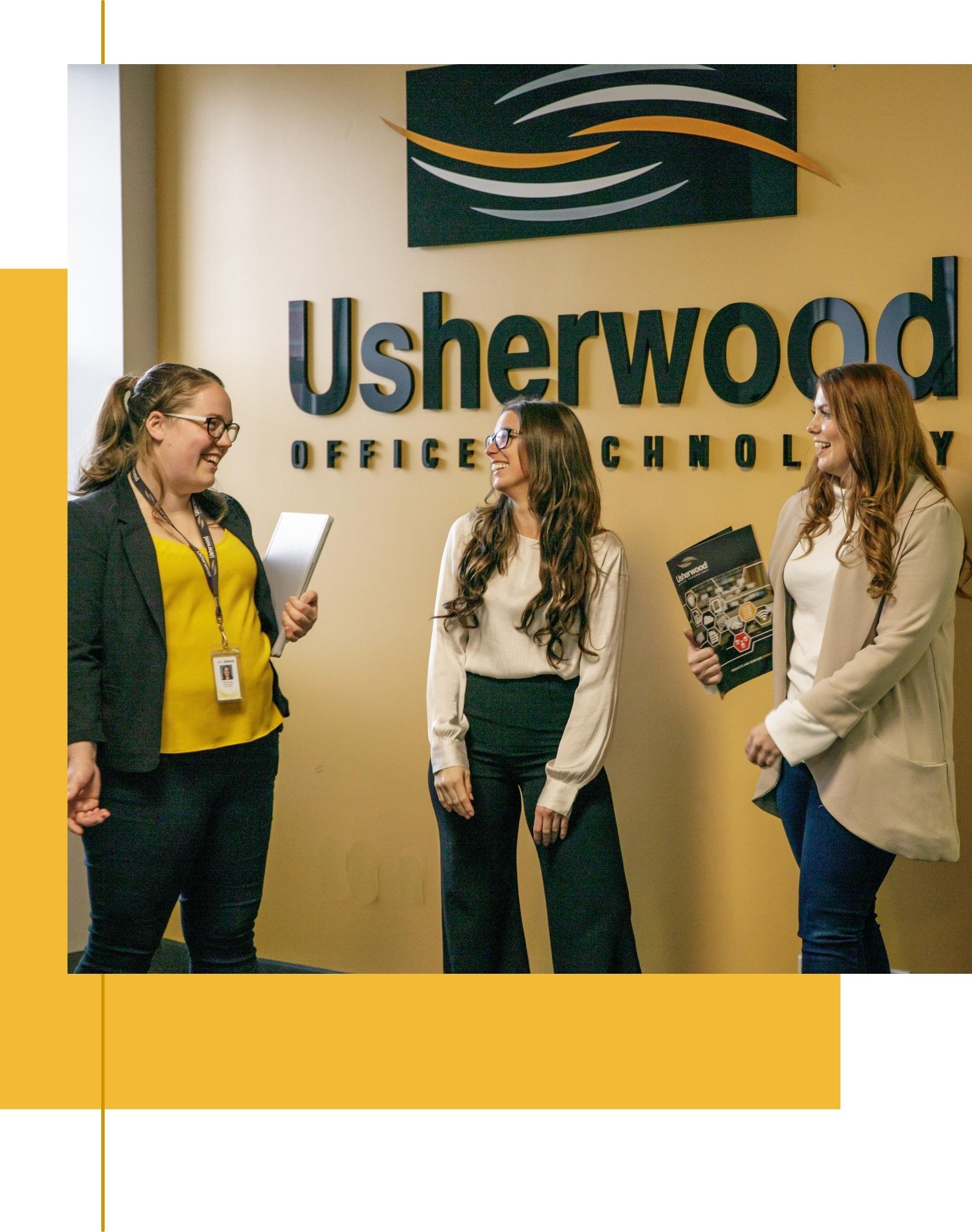 Three women employees standing, talking and smiling in front of Usherwood sign