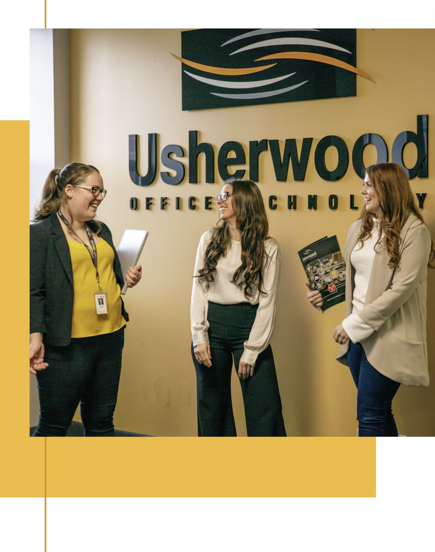 Three women employees standing in front of Usherwood sign talking and smiling