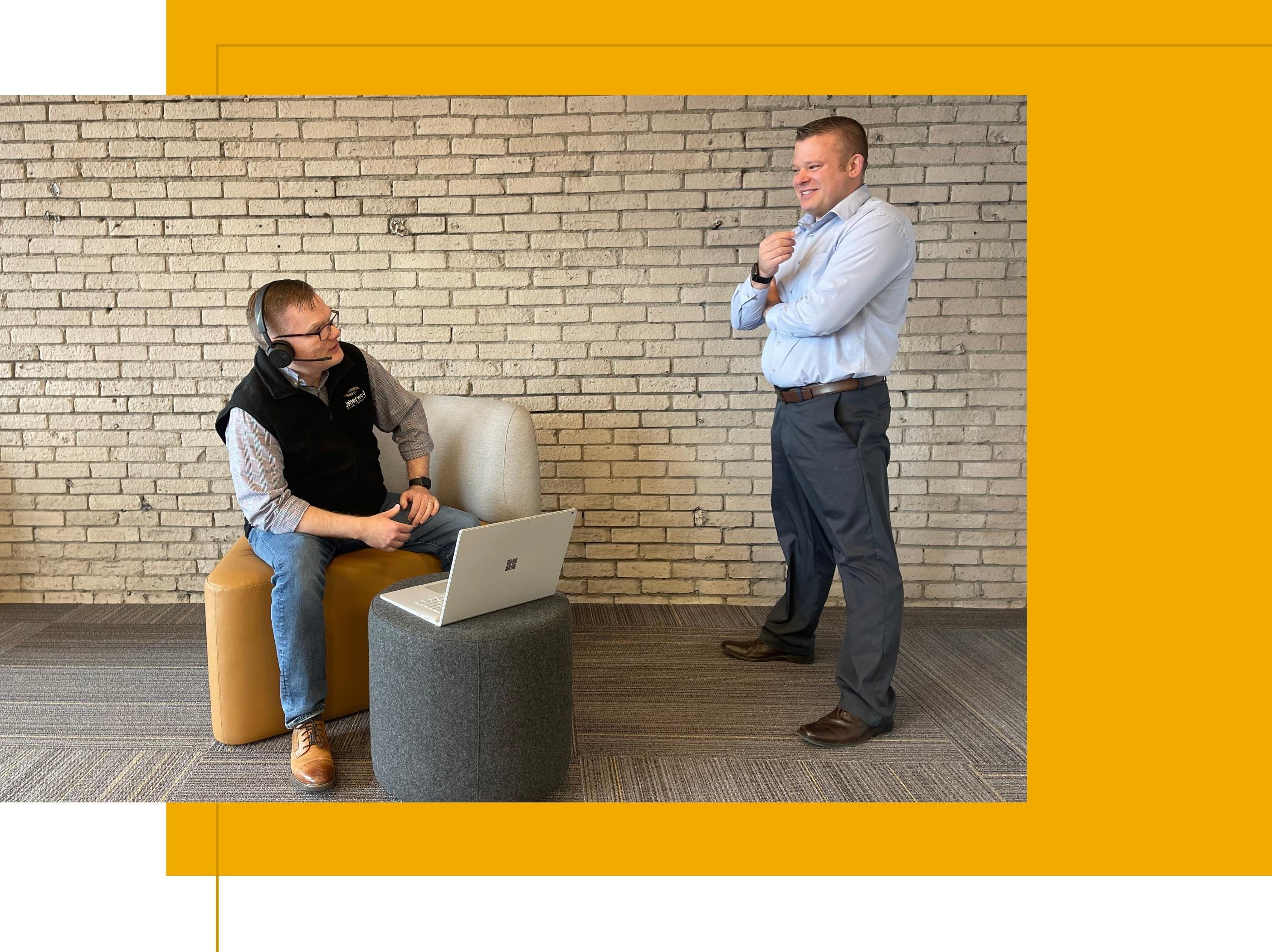 Male employee sitting and talking to standing male employee