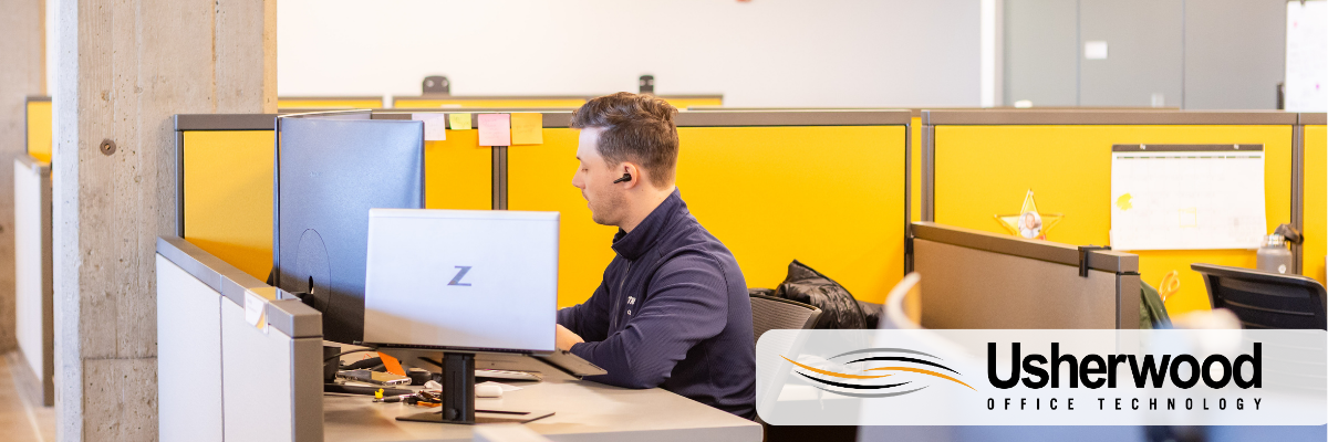 Man at desk with 3 computers and earpiece in demonstrating using cloud communications